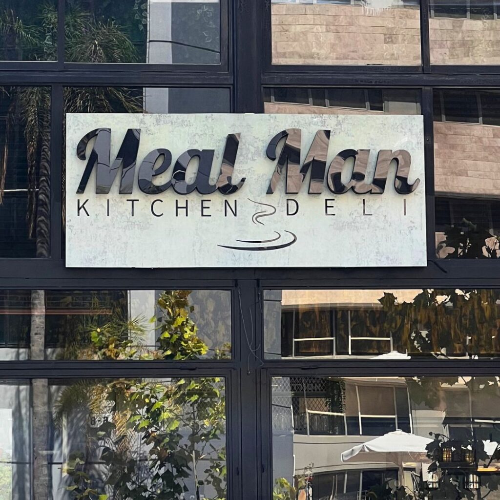 תמונת המסעדה מבחוץ, חלונות עם השתקפויות מבחוץ ושלט עם שם המסעדה mealman