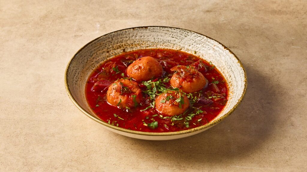 מרק קובה סלק בצלחת עמוקה לבנה על גבי רקע בז׳