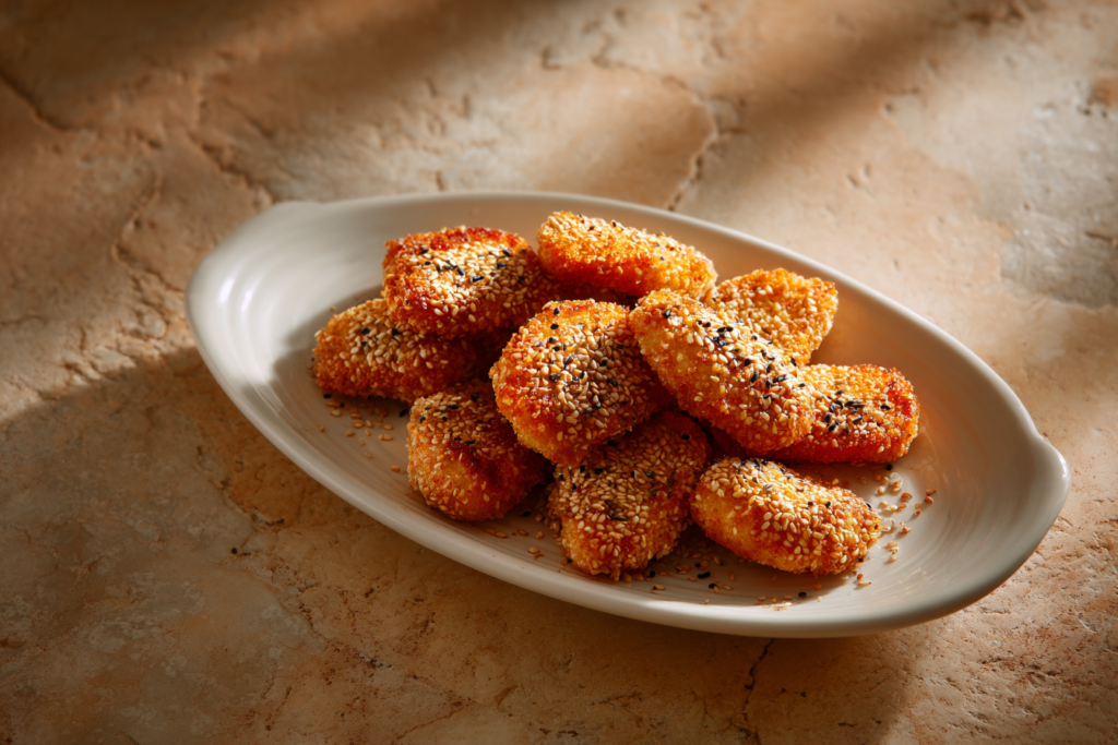 שניצלונים בשומשום בצלחת אובלית לבנה על גבי רקע בז׳