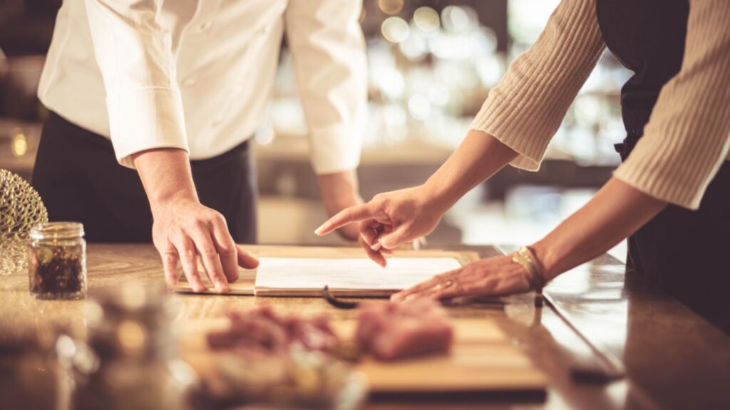 מתכננים ארוע, לקוחה ושף מעל דפים על שולחן