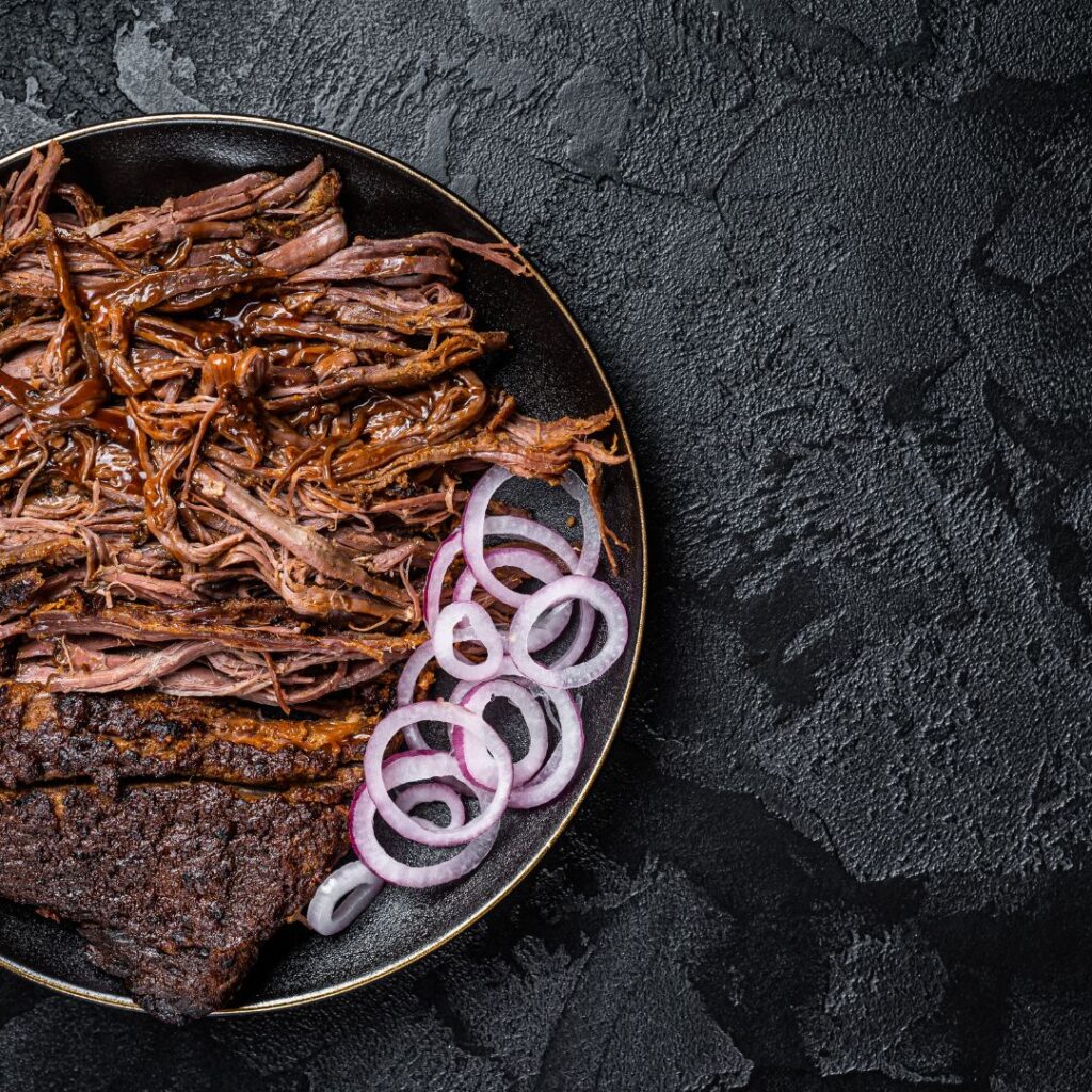 צלחת עם בשר מפורק וטבעות בשר סגול על גבי משטח שיש שחור