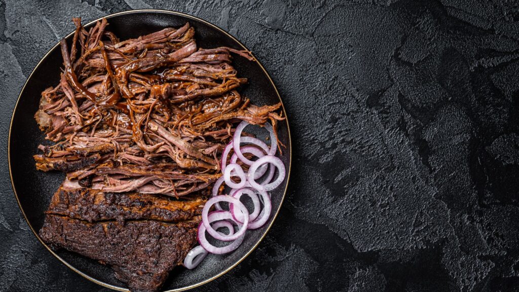 צלחת עם בשר מפורק ובצל סגול על רקע שיש שחור