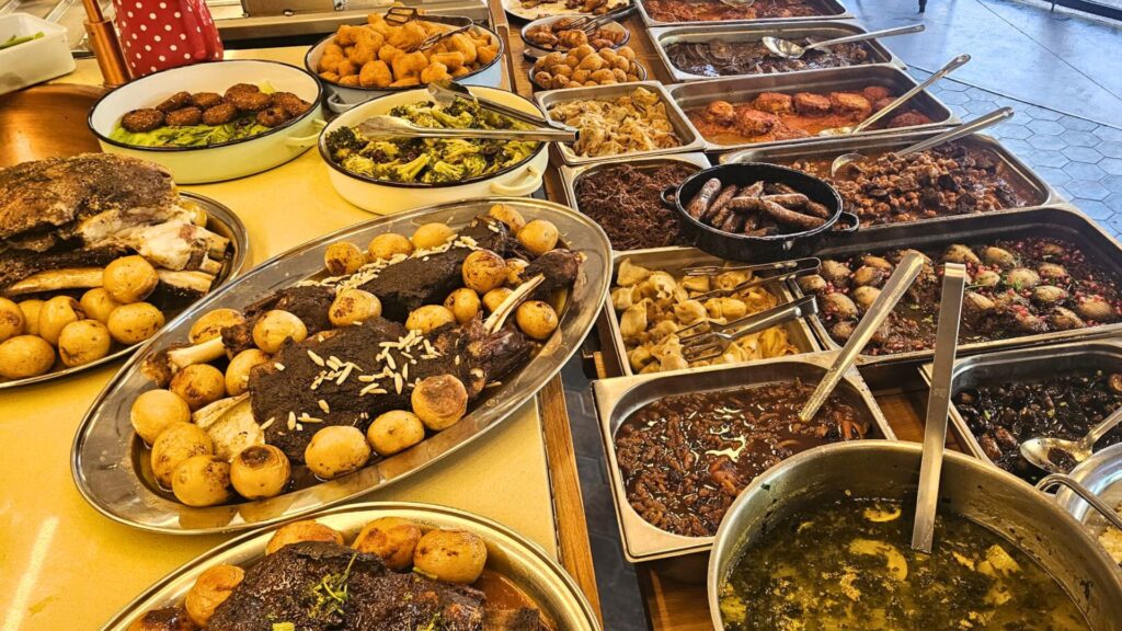 שולחן מעדניה עשיר עם מאכלים לשבת, בשר אסאדו עם תפוחי אדמה מדורה, תבשילים ביתיים, סלטים, תוספות מרקים