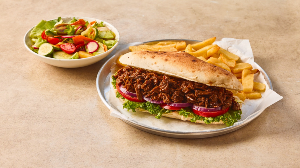 כריך ג'בטה או לחמנייה ארוכה עם פרוסות בשר מעושן/פרוס, חסה, עגבנייה ובצל סגול, מוגש על מגש מתכת עם צ'יפס זהוב וקערת סלט ירקות בצד